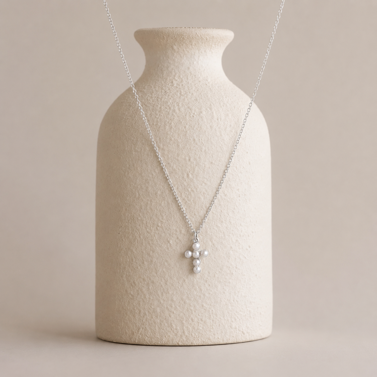 Necklace with a pendant on a textured beige vase against a plain background